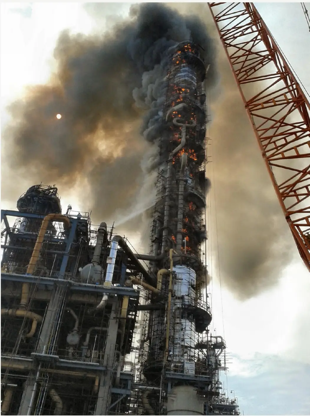 A distillation column engulfed in smoke and flame during a refinery loss-of-containment fire