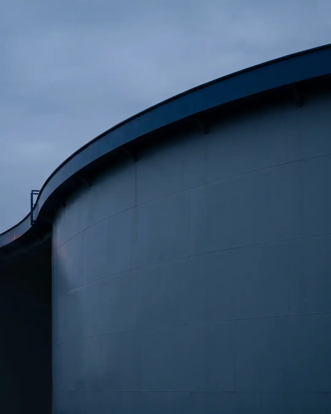 The rim and shell curve of a large floating-roof storage tank at dusk