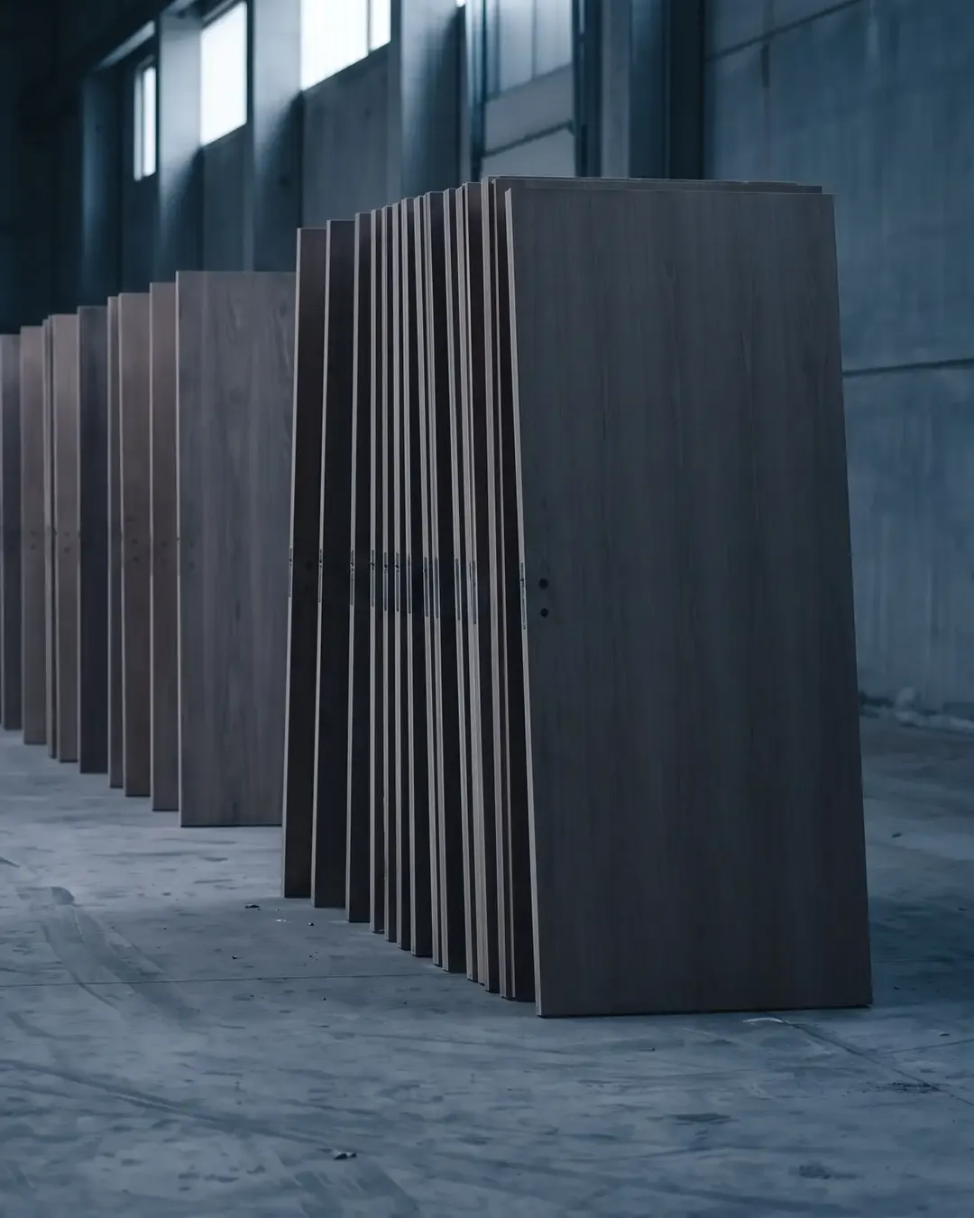 Unfinished flush door shutters standing on edge in a dim hall, receding into shadow