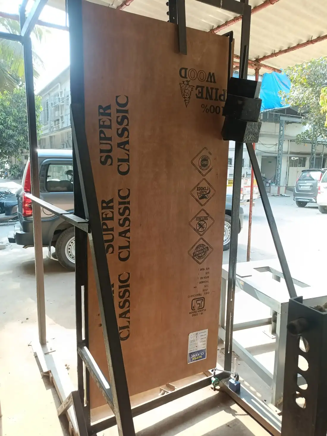 A flush door shutter standing in a steel test frame, its face carrying the manufacturer's IS 2202 marking