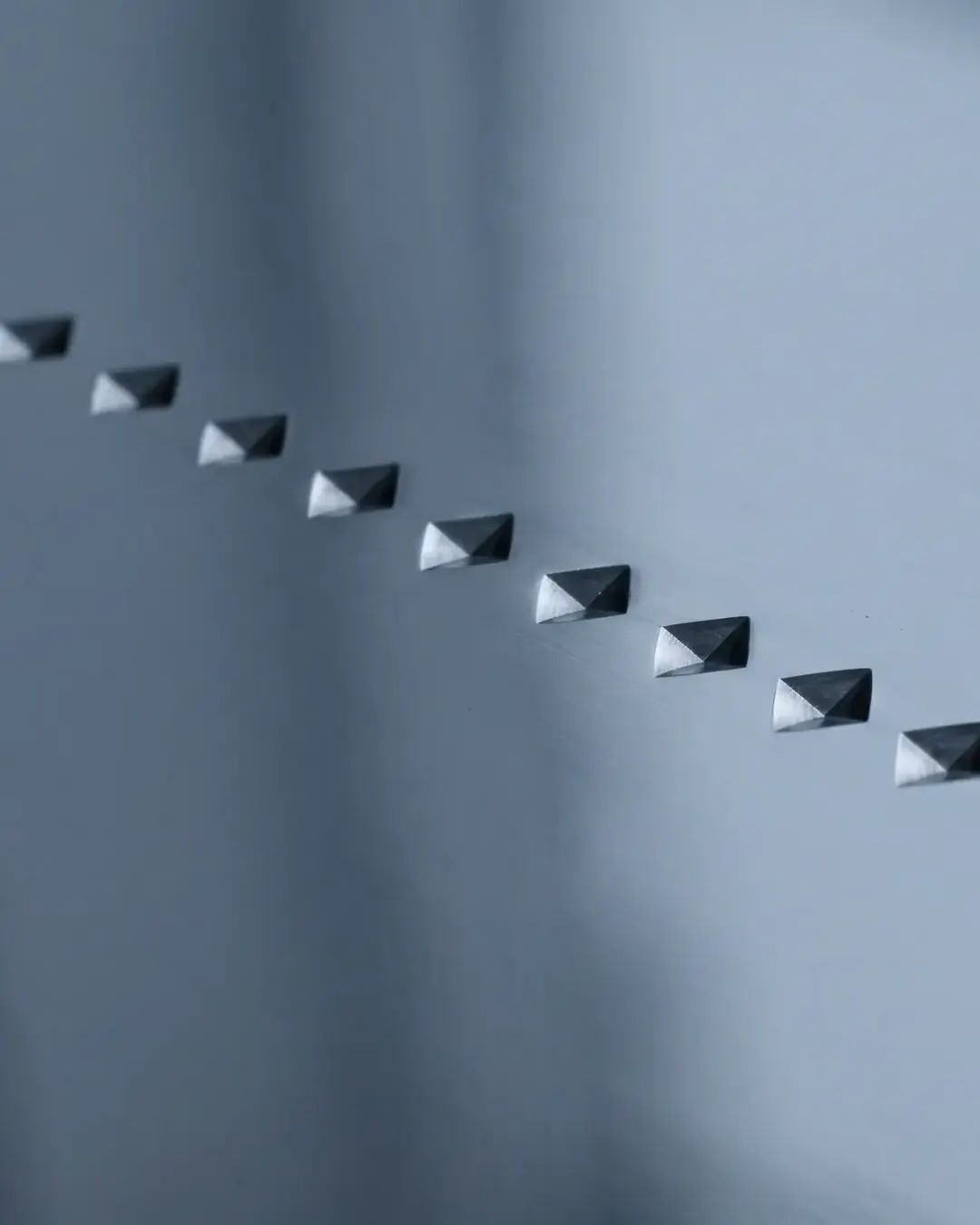 A row of diamond-shaped microhardness indentations across a polished metal surface