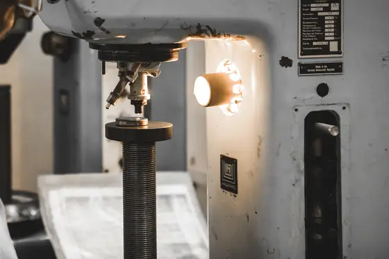 The indenter head and anvil of a bench hardness tester at TCR Engineering, lit by the machine's own lamp
