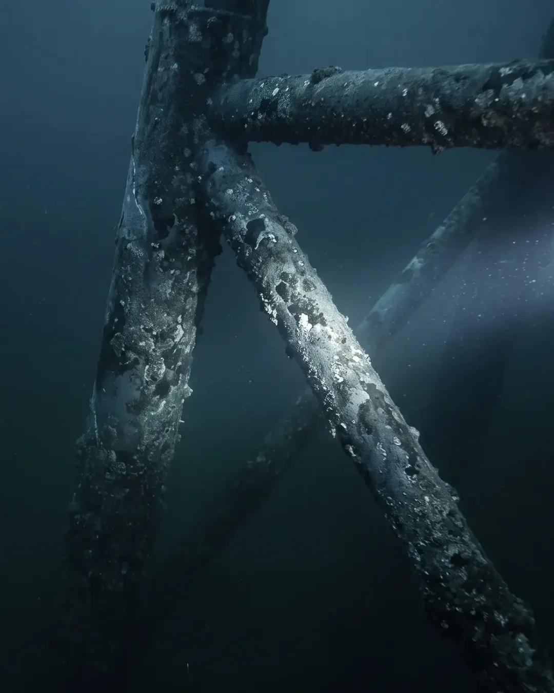 A submerged jacket leg lit by a cold beam in dark water