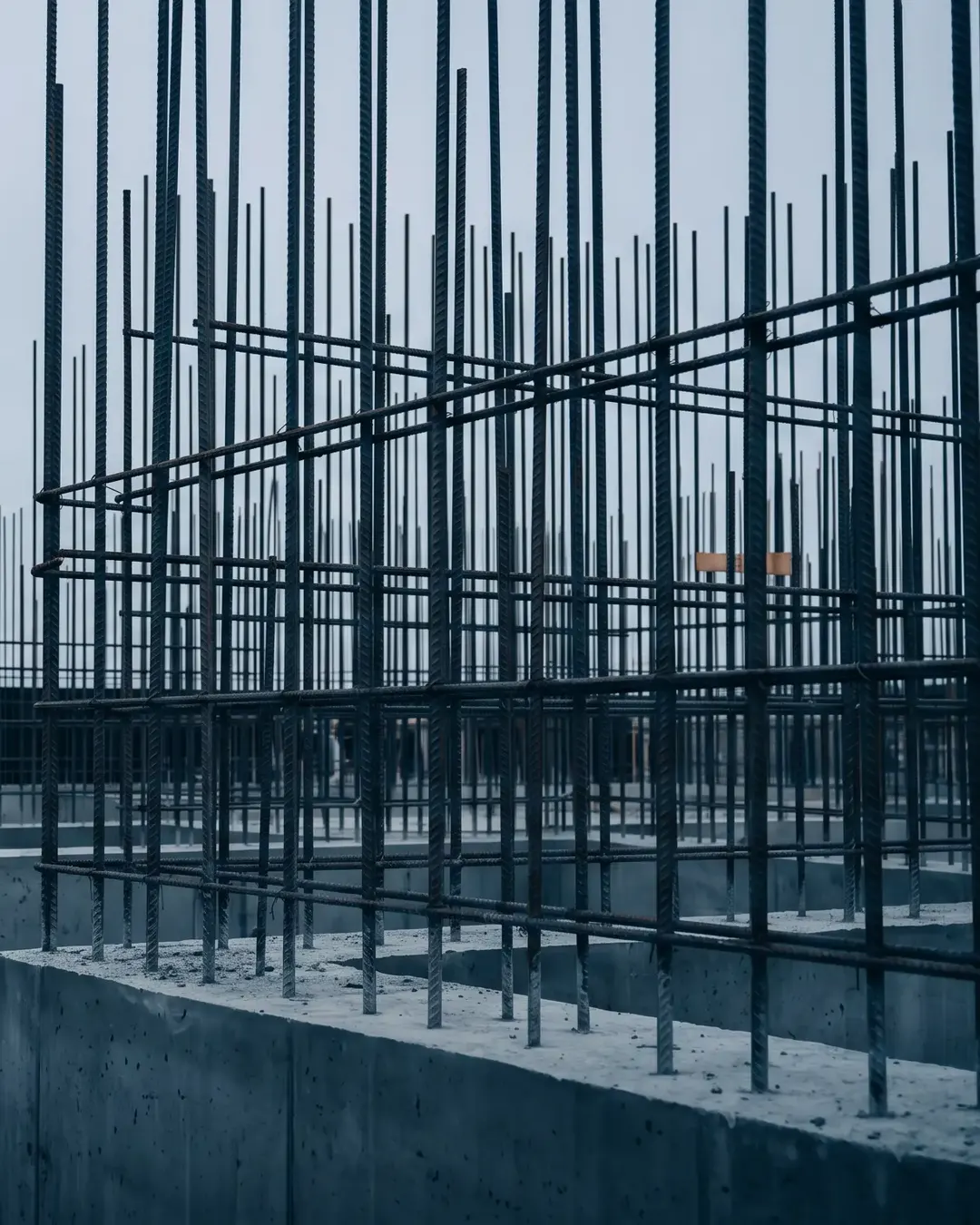 A grid of exposed reinforcement bars rising from a fresh raft foundation