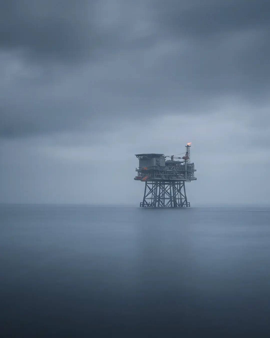 A fixed offshore jacket platform seen from sea level through cold haze, reduced to a grey lattice