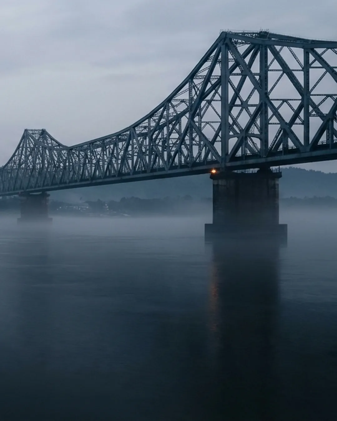 The Brahmaputra at Guwahati at dawn: the Saraighat cantilever bridge crossing still water, forested hills receding behind it