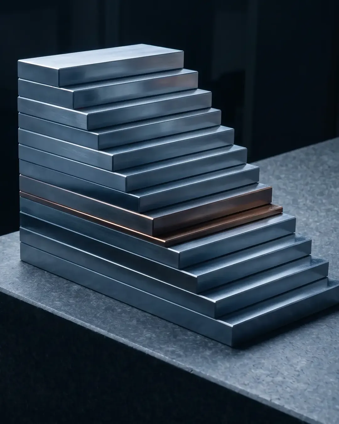 A stepped stack of precision gauge blocks on a granite surface plate under raking light