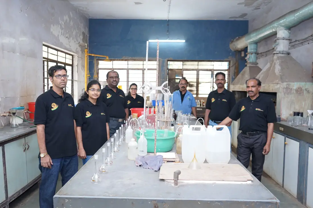 Eight TCR Engineering laboratory staff standing at the wet chemistry bench, volumetric flasks, filtration funnels and wash bottles set out in front of them