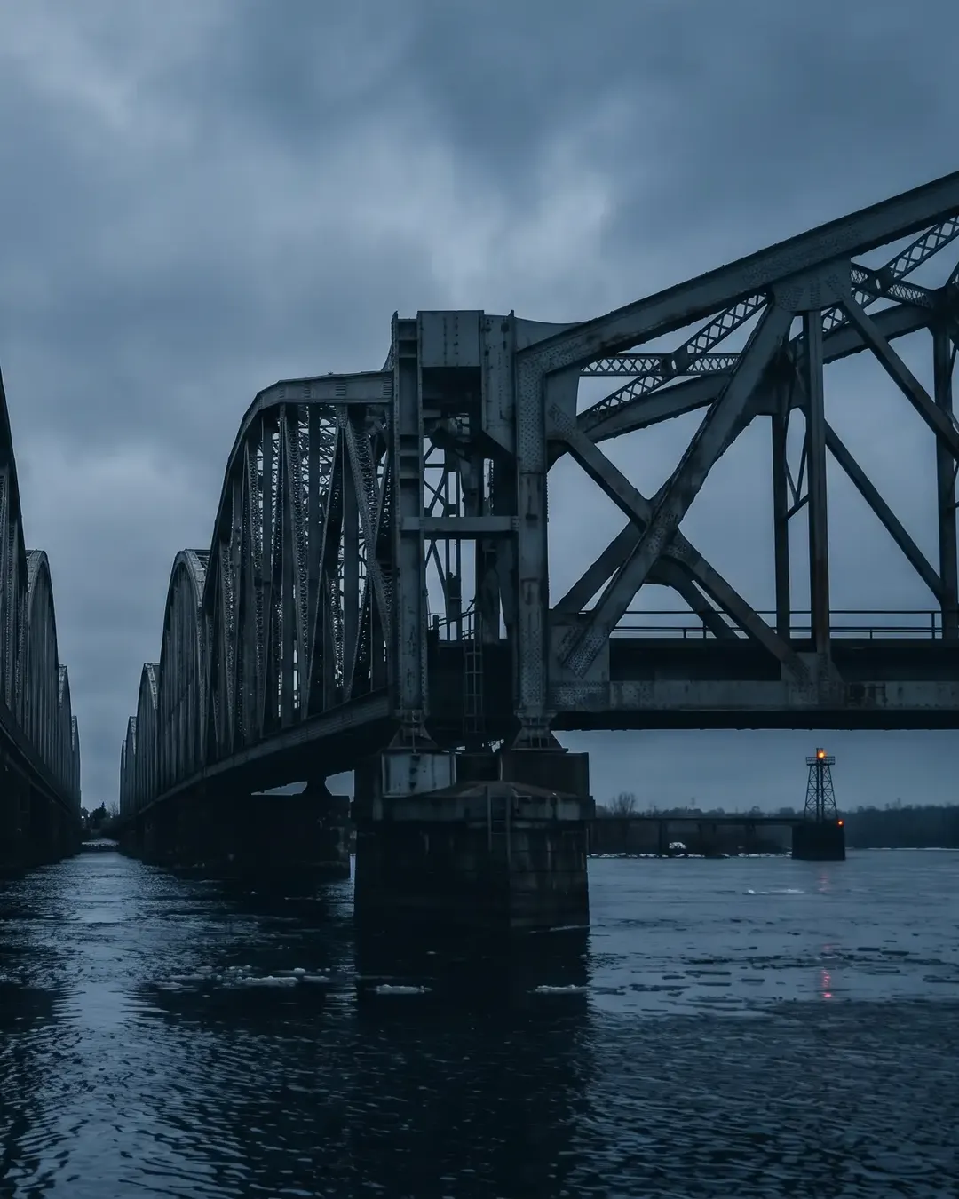 Two steel truss bridge sections meeting at mid-span over cold water at dawn