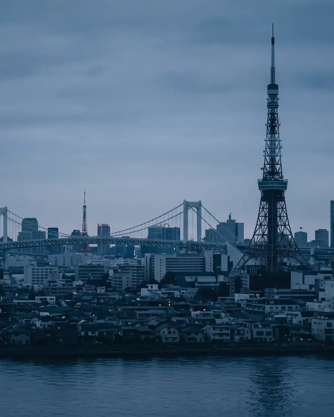 Tokyo at blue hour from across the bay: Tokyo Tower and the Rainbow Bridge above the low city