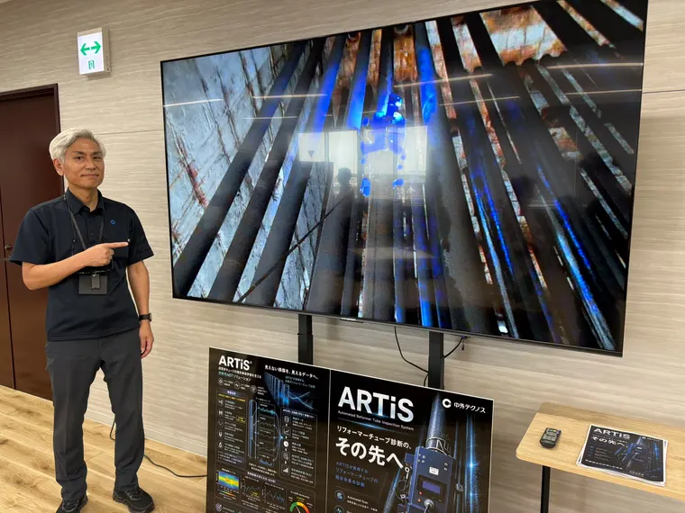 Naoshi Kawabe of Chugai Technos presenting the ARTiS reformer tube inspection system, with the crawler shown climbing a radiant tube on the screen behind him and the Japanese-language ARTiS flyer and stand poster alongside