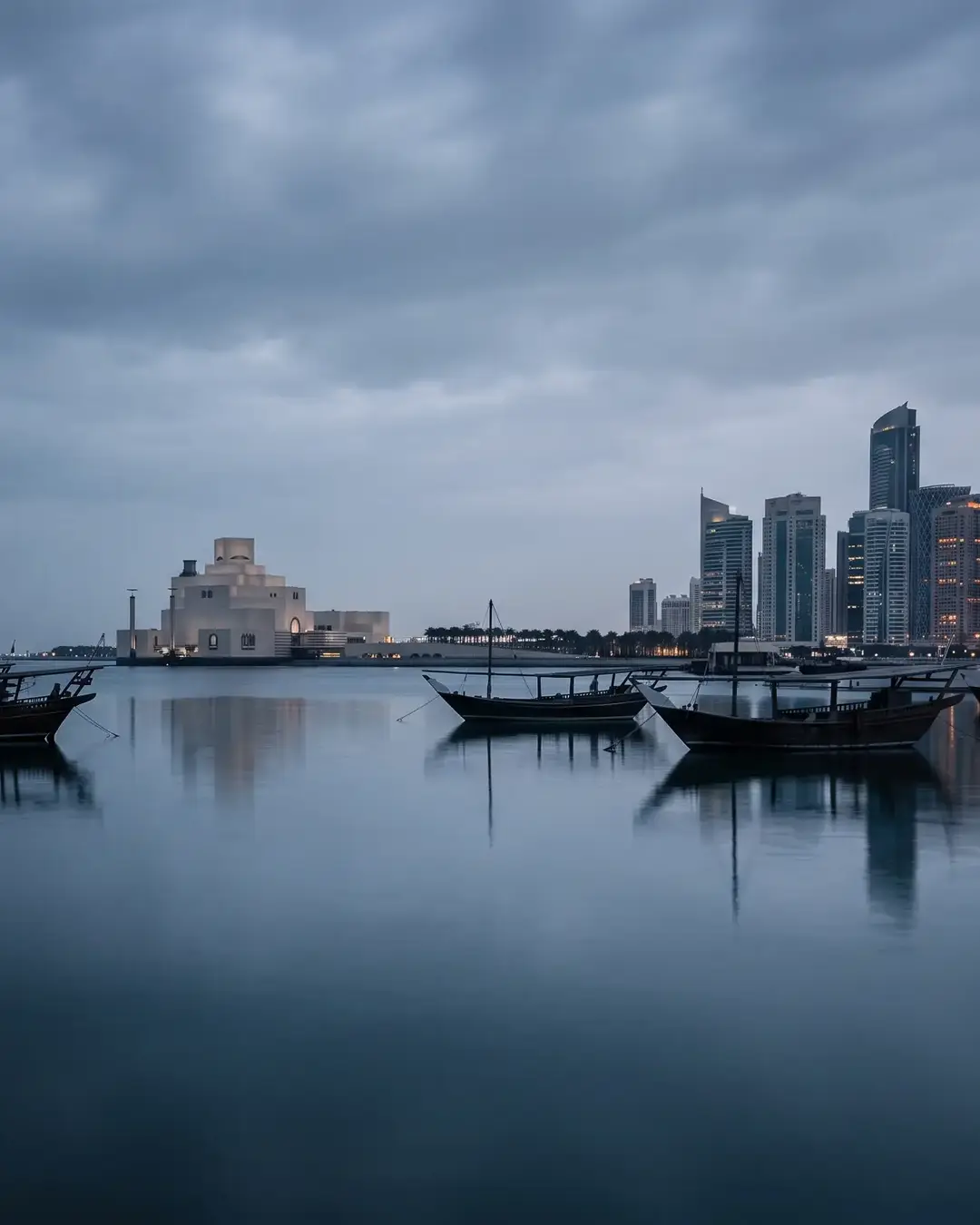 Doha at blue hour: dhows moored on the Corniche, the Museum of Islamic Art on its island, and the West Bay towers beyond