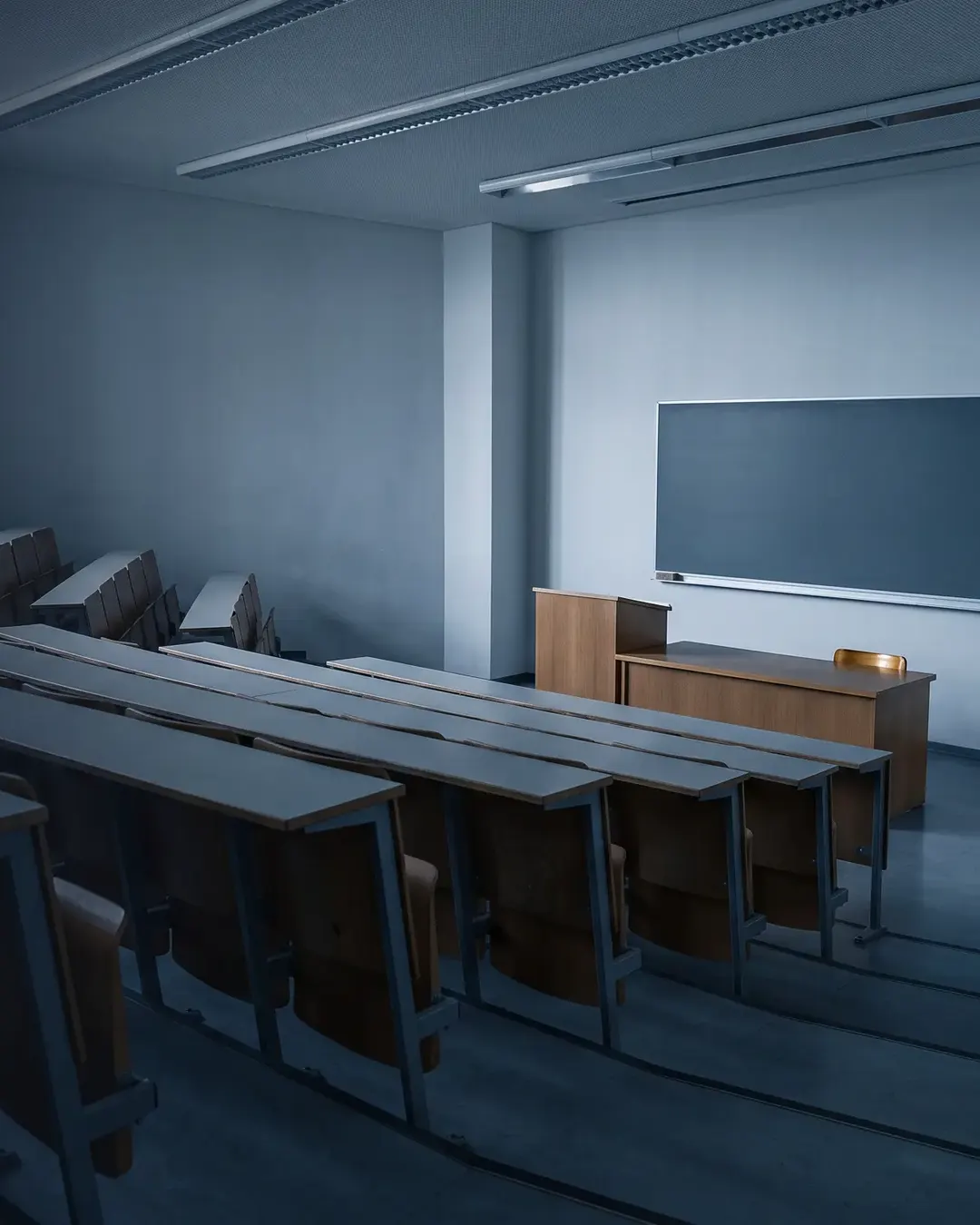 An empty tiered lecture room in cold morning light, rows of plain desks receding