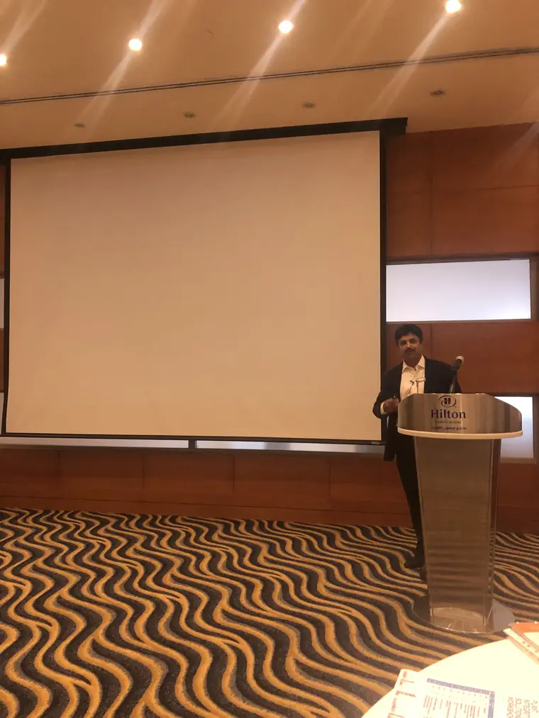 Paresh Haribhakti at the Hilton lectern between slides, the projection screen alongside him